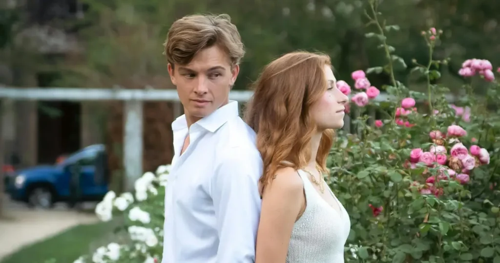 Paar lehnt Rücken an Rücken vor Rosen, Stimmung wirkt angespannt.