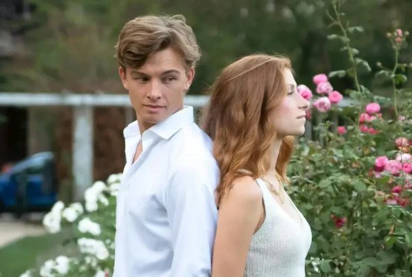 Paar lehnt Rücken an Rücken vor Rosen, Stimmung wirkt angespannt.