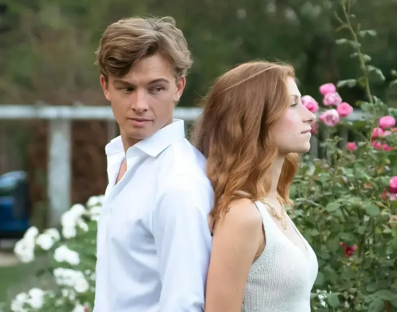 Paar lehnt Rücken an Rücken vor Rosen, Stimmung wirkt angespannt.