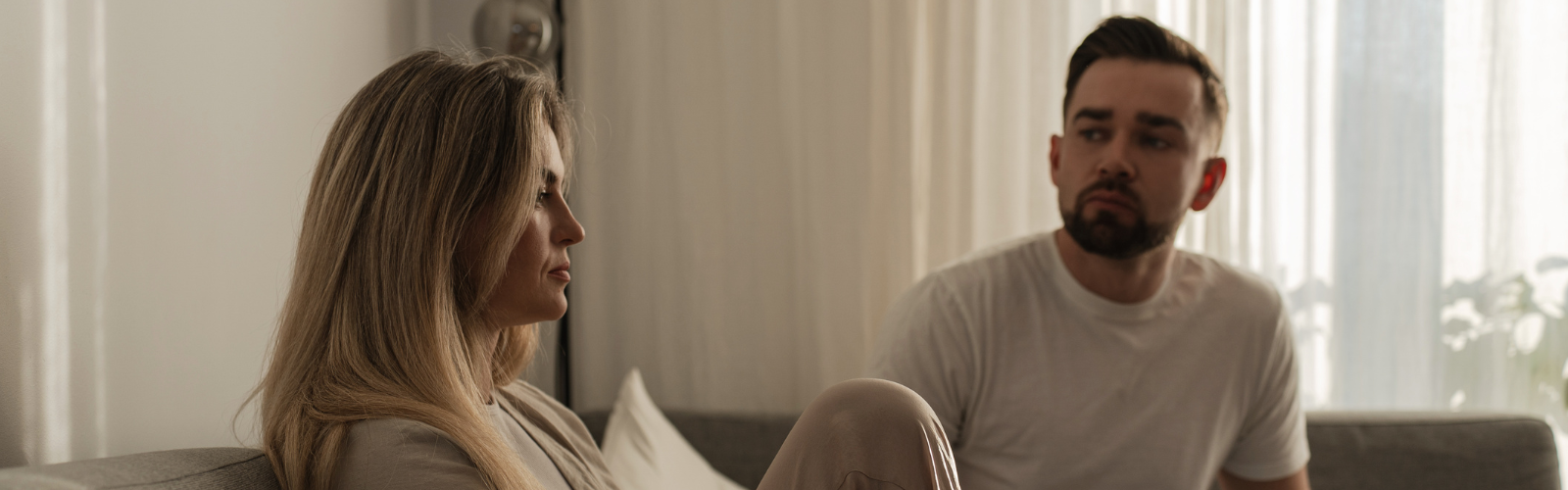 Paar sitzt mit ernsten Gesichtern distanziert auf dem Sofa.