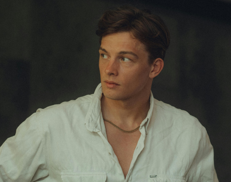 junger Mann im weißen Hemd, der seitlich blickt; Porträt von Brust aufwärts gerahmt.