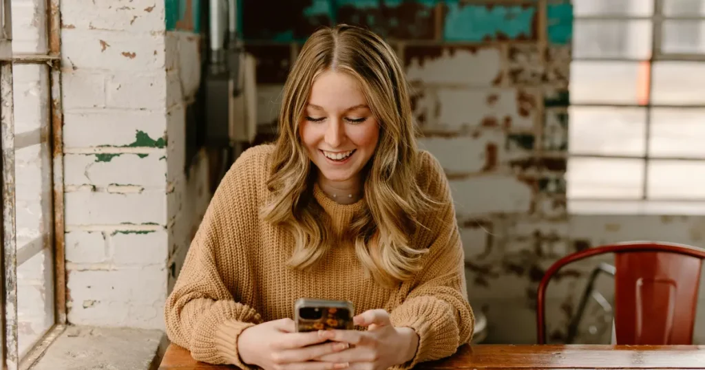 Junge Frau liest lachend eine Textnachricht.