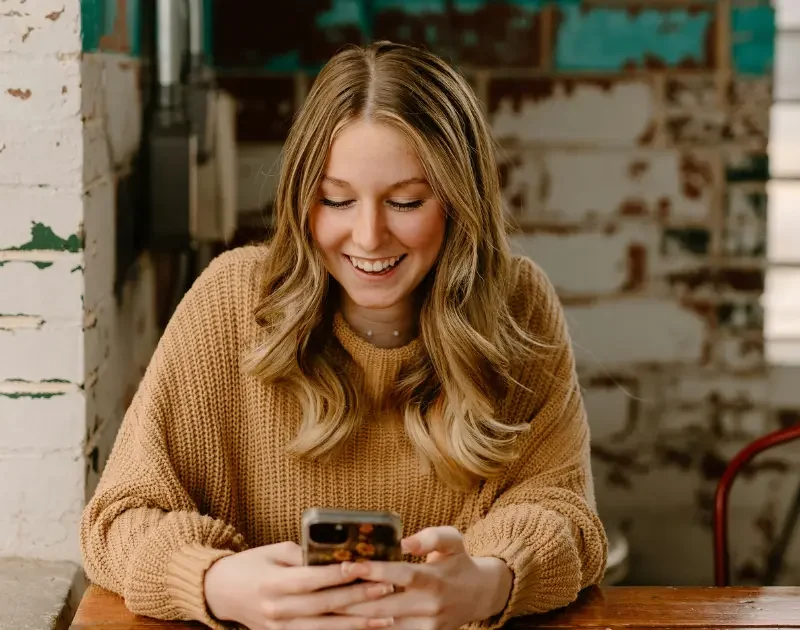 Junge Frau liest lachend eine Textnachricht.