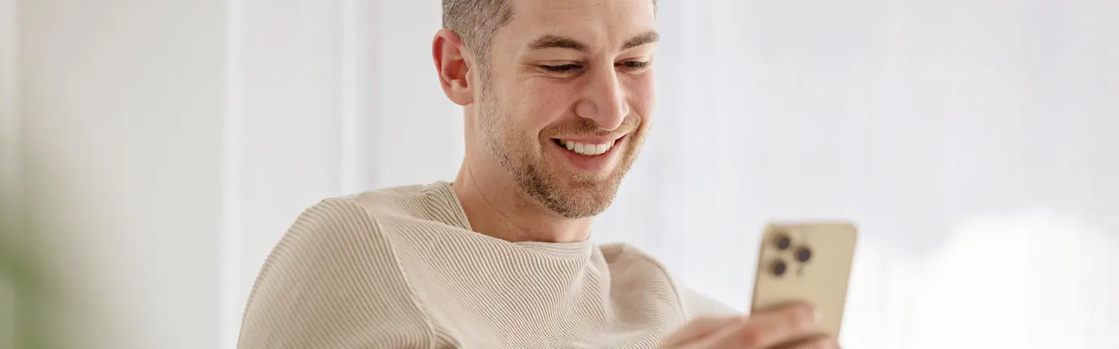 Mann lächelt beim Chatten auf goldenem Smartphone.