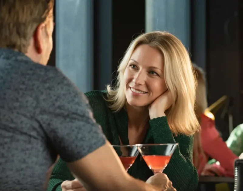 Frau lächelt Mann beim Cocktail-Date in einer Bar an.