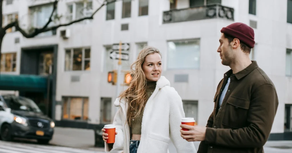 Paar läuft mit Kaffee in der Hand durch eine belebte Stadt.