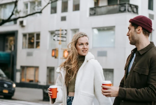 Paar läuft mit Kaffee in der Hand durch eine belebte Stadt.