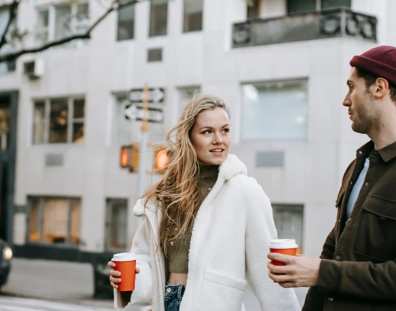Paar läuft mit Kaffee in der Hand durch eine belebte Stadt.