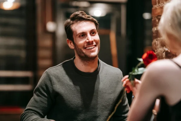 Lächelnder Mann schaut Frau mit roter Rose an.