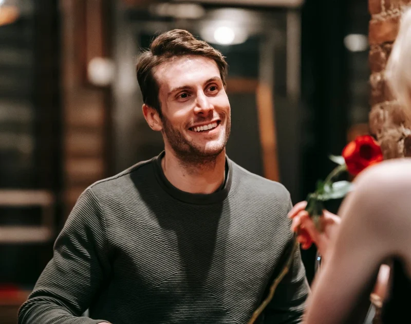 Lächelnder Mann schaut Frau mit roter Rose an.