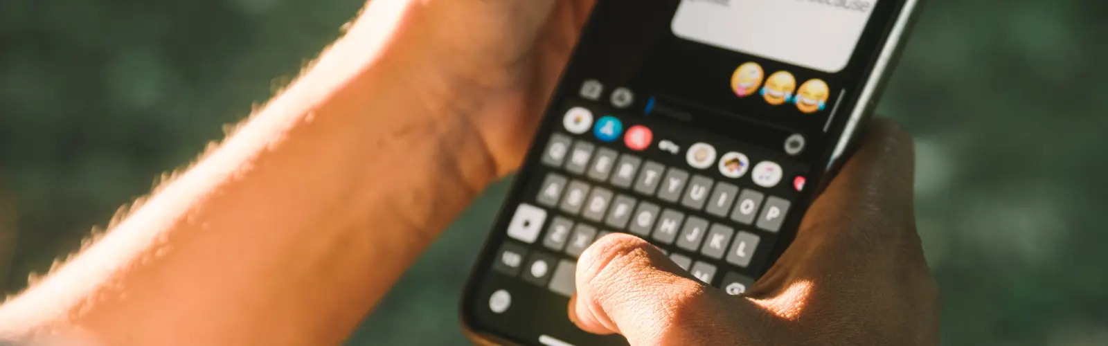 Nahaufnahme von Händen, die Emojis in einer Textnachricht tippen.