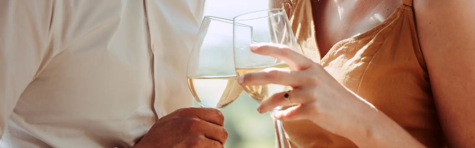 Nahaufnahme eines Paares, das mit Weißwein anstößt.