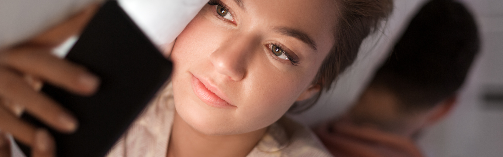 Nachdenkliche Frau liegt im Bett und schaut auf ihr Smartphone.