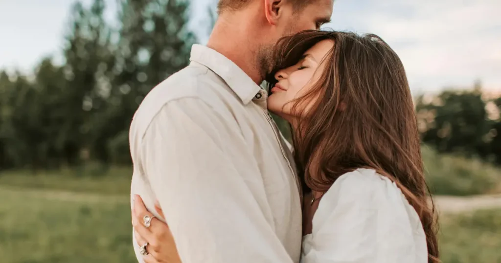 Mann und Frau in inniger Umarmung auf einer Wiese, die Geborgenheit und tiefe Verbindung darstellt.