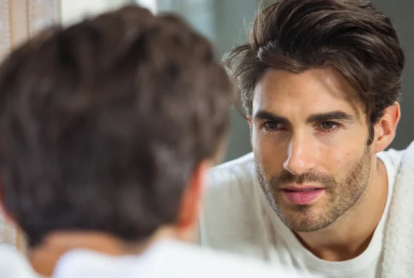 Ein attraktiver Mann betrachtet sein Spiegelbild im Badezimmer, was die Selbstbezogenheit eines Narzissten symbolisiert.