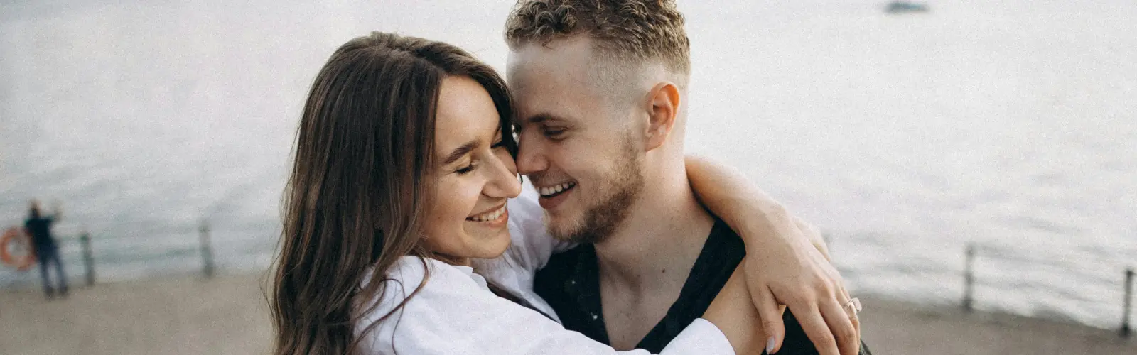 Lächelndes Paar in enger Umarmung am Wasser, als Symbol für das Meistern einer Beziehungskrise.