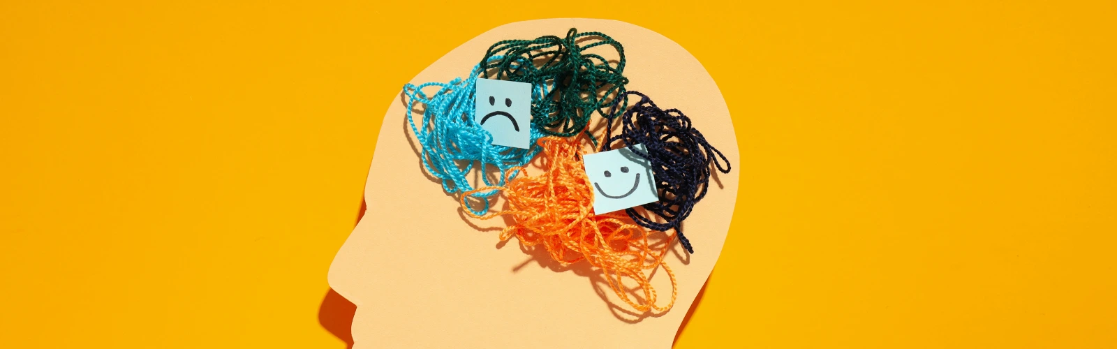 Illustration eines menschlichen Kopfes mit bunten, verhedderten Fäden und Smileys, die das Gefühlschaos bei Persönlichkeitsstörungen darstellen.