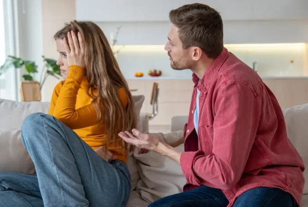 Ein Mann versucht verzweifelt mit einer Frau zu sprechen, die ihn ignoriert und sich gestresst an den Kopf fasst.