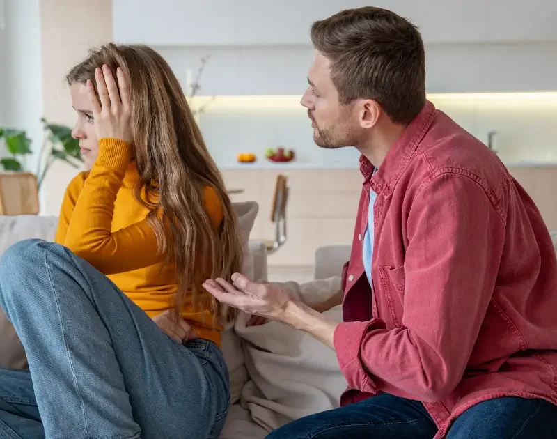 Ein Mann versucht verzweifelt mit einer Frau zu sprechen, die ihn ignoriert und sich gestresst an den Kopf fasst.