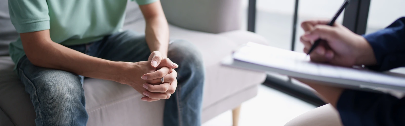 Nahaufnahme einer Therapiesitzung, bei der ein Mann auf dem Sofa sitzt und ein Therapeut Notizen zu seinem Verhalten macht.