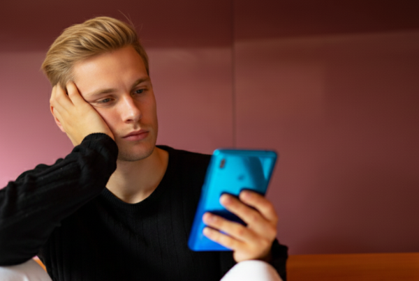 Mann schaut nachdenklich auf sein Handy und fragt sich, warum sie ihn ignoriert, obwohl Interesse da ist