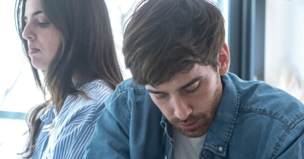 Paar sitzt emotional distanziert nebeneinander, ein Mann wirkt zurückgezogen – typisches Anzeichen von Bindungsangst