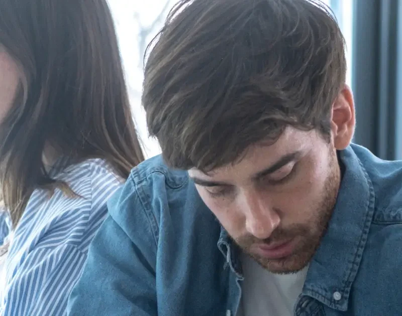 Paar sitzt emotional distanziert nebeneinander, ein Mann wirkt zurückgezogen – typisches Anzeichen von Bindungsangst