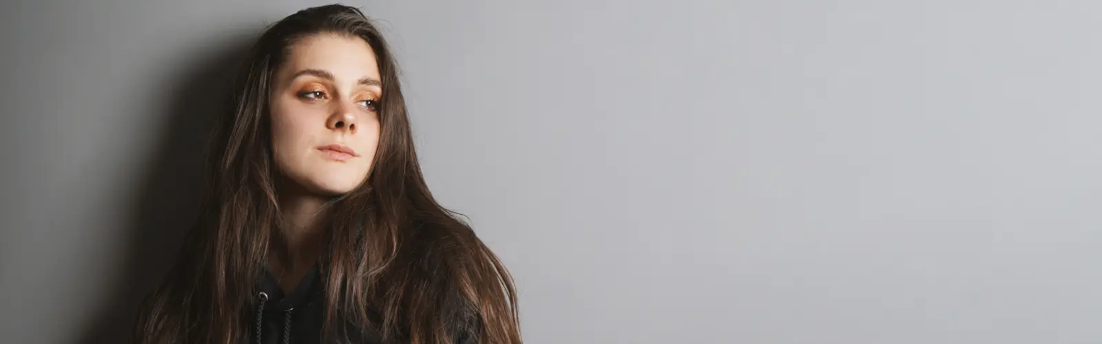 Porträt einer jungen Frau mit langem braunem Haar, die nachdenklich und ausweichend zur Seite blickt.