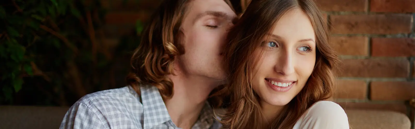 Paar sitzt eng beieinander, Mann lehnt sich liebevoll an Frau an