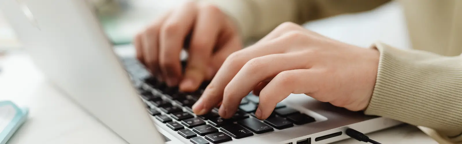 Nahaufnahme von Händen, die konzentriert auf einer silbernen Laptop-Tastatur tippen.