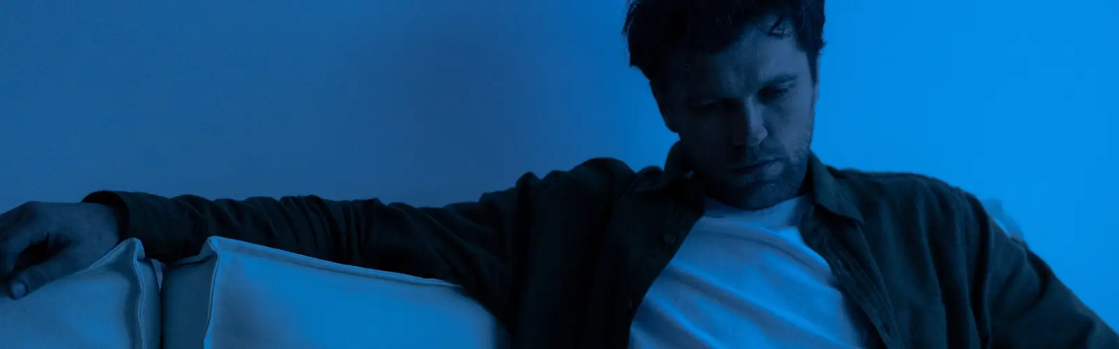 Nachdenklicher Mann sitzt allein auf dem Sofa – häufiges Symptom von Bindungsangst beim Mann