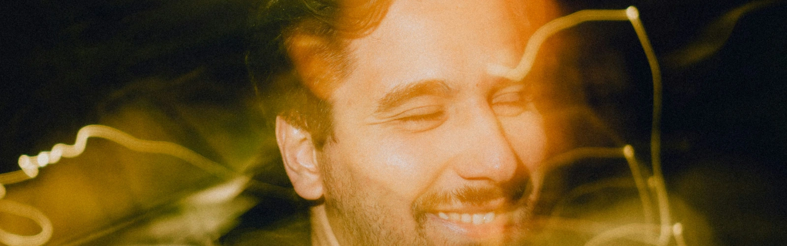 Ein lächelnder Mann mit geschlossenen Augen in einer verschwommenen Lichtatmosphäre, der emotionale Heilung und Befreiung von Liebeskummer verkörpert.