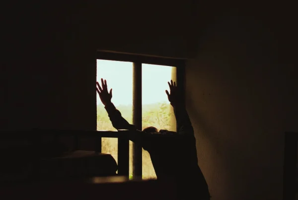 Silhouette eines verzweifelten Mannes, der seine Hände gegen ein Fenster drückt, als Symbol für den Schmerz während der ersten Phase des Liebeskummers.