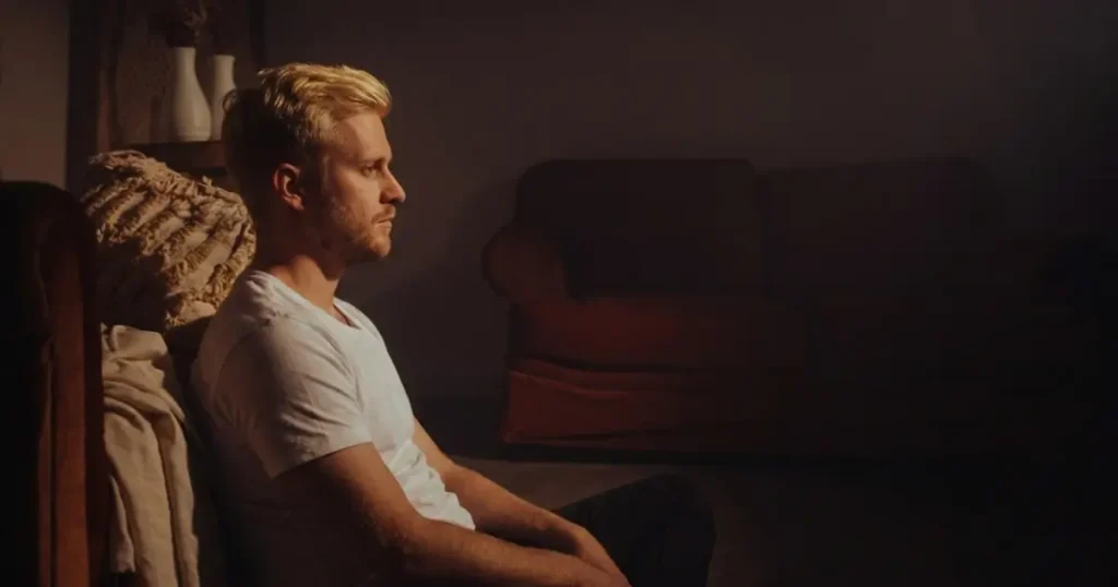 Ein nachdenklicher Mann sitzt allein im gedimmten Licht auf dem Boden und starrt ins Leere, was die emotionale Isolation nach einer Trennung symbolisiert.
