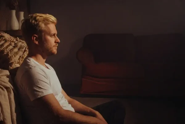 Ein nachdenklicher Mann sitzt allein im gedimmten Licht auf dem Boden und starrt ins Leere, was die emotionale Isolation nach einer Trennung symbolisiert.