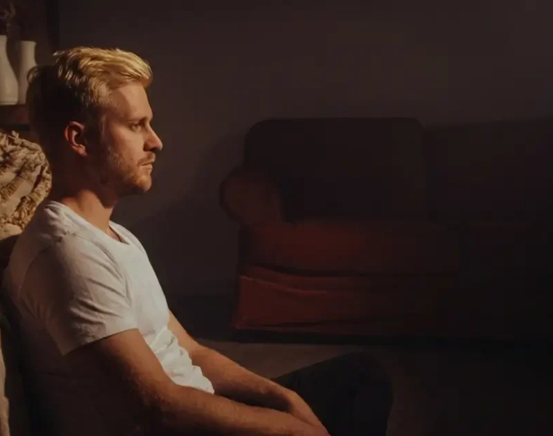 Ein nachdenklicher Mann sitzt allein im gedimmten Licht auf dem Boden und starrt ins Leere, was die emotionale Isolation nach einer Trennung symbolisiert.