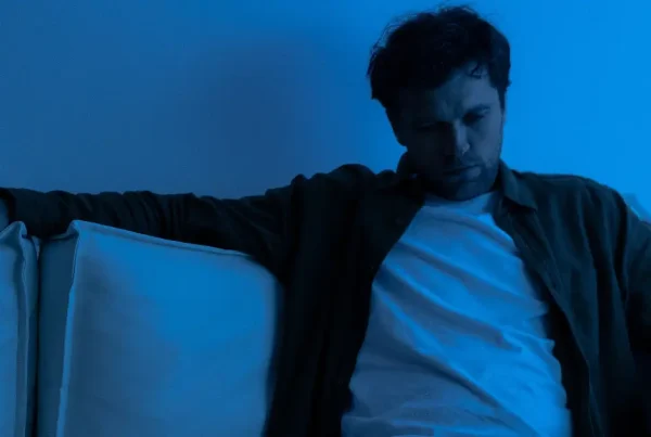 Nachdenklicher Mann sitzt allein auf dem Sofa in blauem Licht, Sinnbild für emotionale Rückfälle.